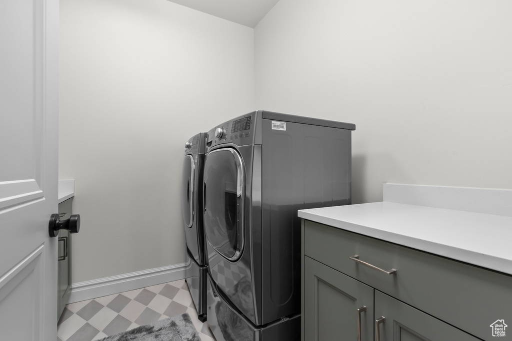 Washroom featuring washing machine and clothes dryer, cabinets, and light tile floors