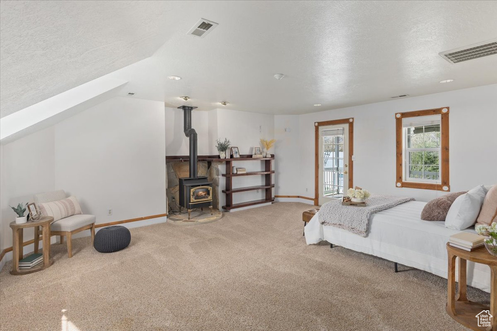 Carpeted bedroom featuring a textured ceiling, a wood stove, and vaulted ceiling
