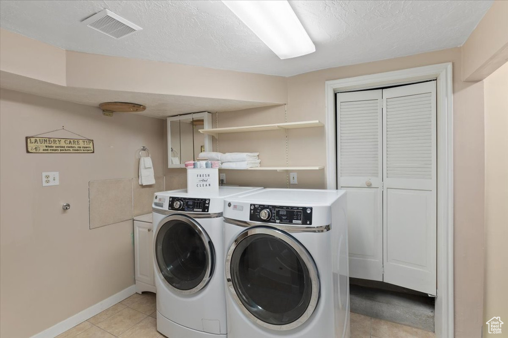 Clothes washing area featuring washing machine and clothes dryer, cabinets, a textured ceiling, and light tile flooring