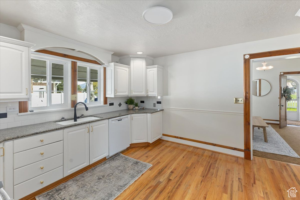 Kitchen with white cabinetry, backsplash, white dishwasher, sink, and light hardwood / wood-style floors