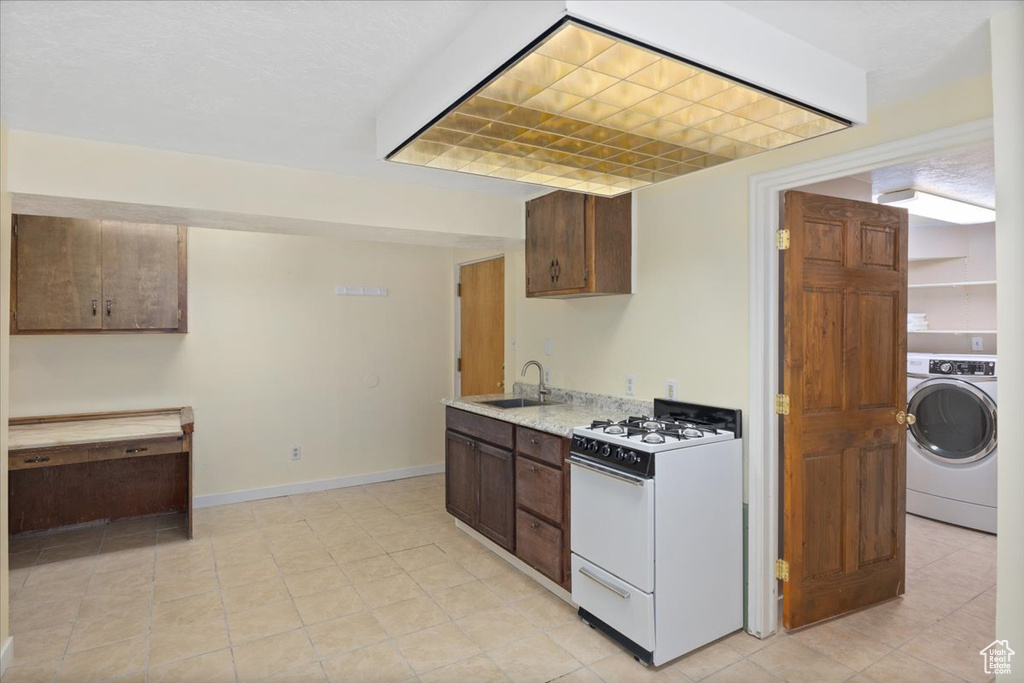 Kitchen featuring gas range gas stove, light tile floors, sink, and washer / dryer