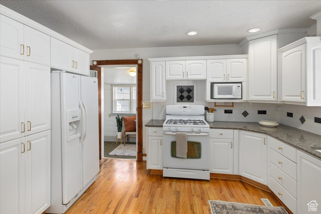 Kitchen with backsplash, white appliances, light hardwood / wood-style floors, dark stone countertops, and white cabinets