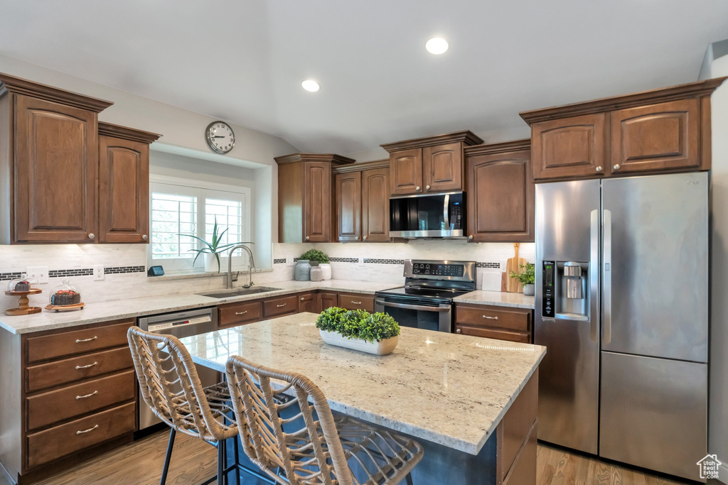 Kitchen with appliances with stainless steel finishes, backsplash, light hardwood / wood-style floors, sink, and a center island