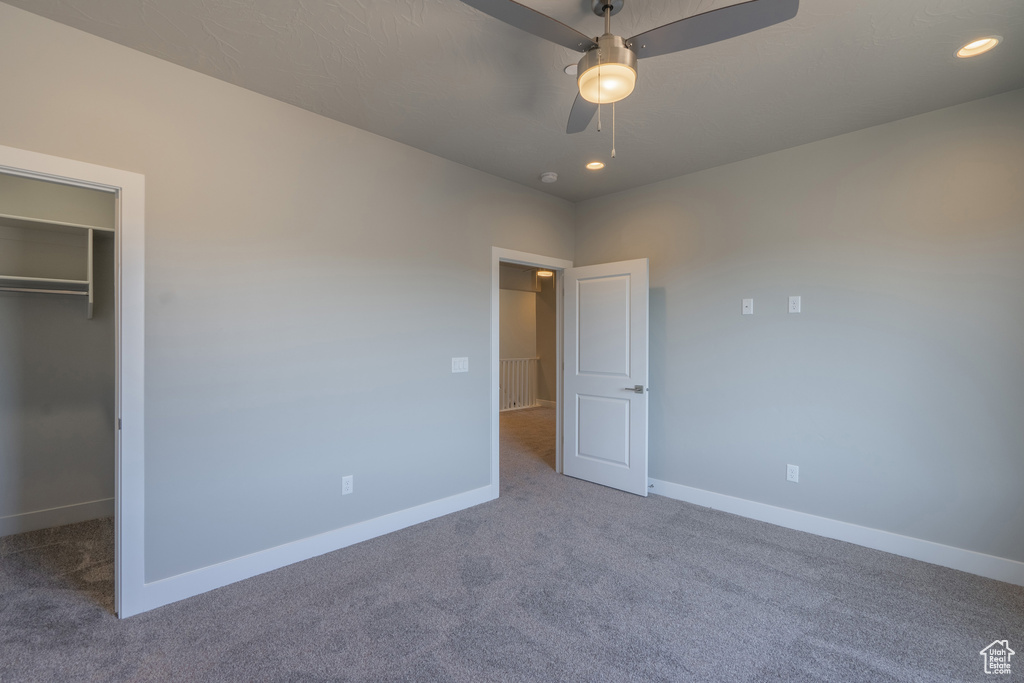 Unfurnished bedroom with a closet, ceiling fan, dark carpet, and a walk in closet