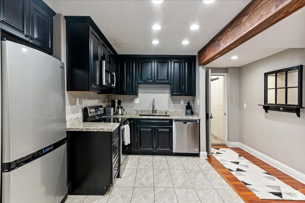 Kitchen with sink, appliances with stainless steel finishes, light tile floors, and light stone counters