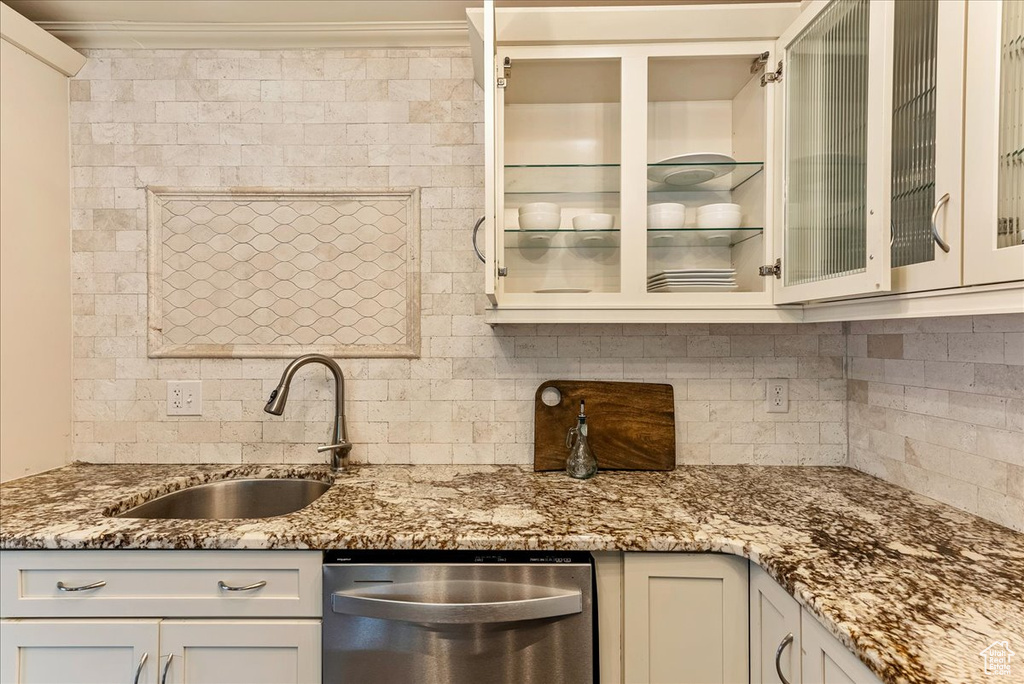 Kitchen with tasteful backsplash, dishwasher, sink, and light stone counters