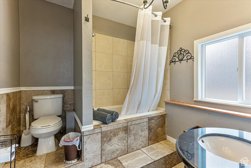 Full bathroom featuring tile walls, shower / bathtub combination with curtain, toilet, sink, and tile floors