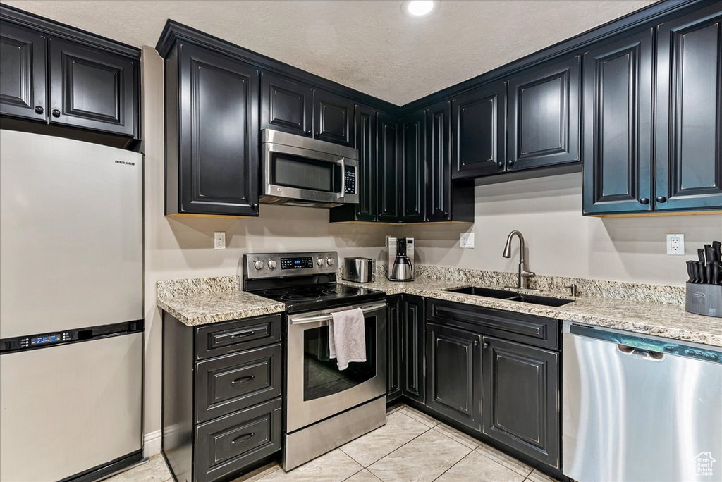Kitchen featuring stainless steel appliances, light tile floors, sink, and light stone counters