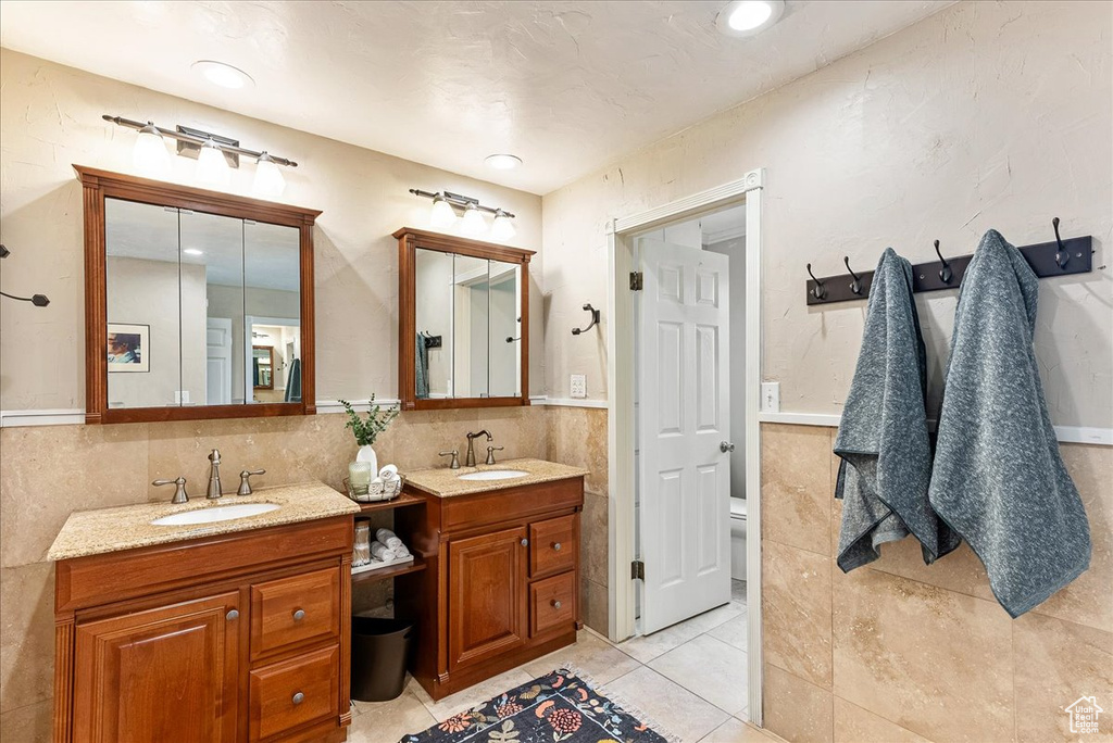 Bathroom featuring tile flooring, tile walls, dual vanity, tasteful backsplash, and toilet