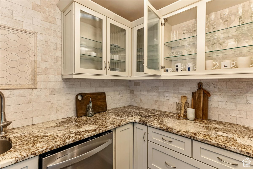 Kitchen featuring dishwasher, tasteful backsplash, white cabinetry, and light stone countertops