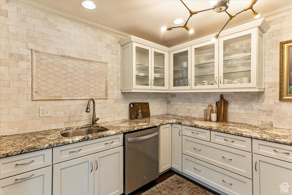 Kitchen with light stone countertops, crown molding, white cabinetry, sink, and stainless steel dishwasher