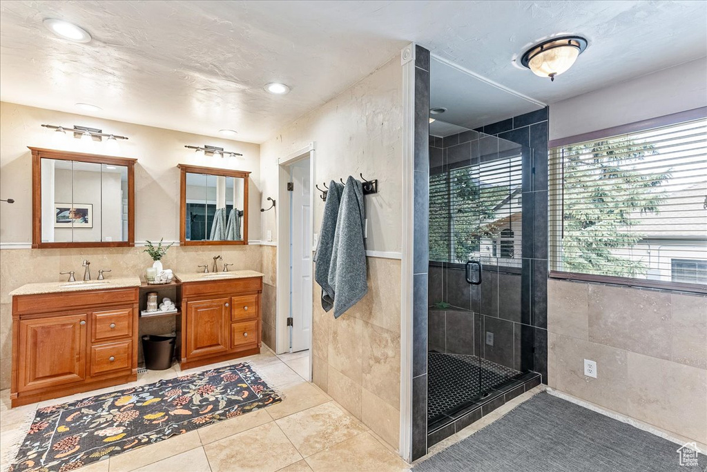 Bathroom featuring walk in shower, vanity with extensive cabinet space, tile floors, tile walls, and double sink