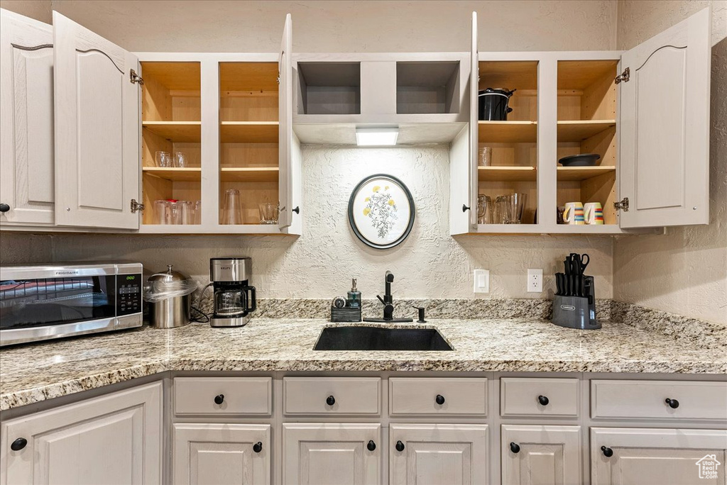 Kitchen featuring white cabinets, sink, and light stone countertops