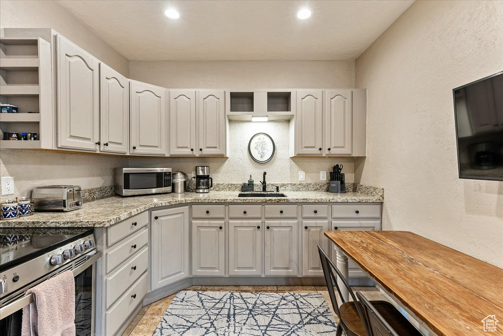 Kitchen with wood counters, stainless steel appliances, white cabinetry, sink, and light tile floors