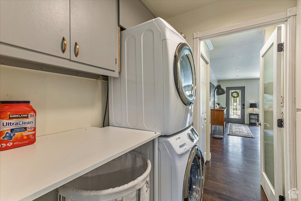 Laundry area with dark hardwood / wood-style flooring, cabinets, and stacked washer and dryer