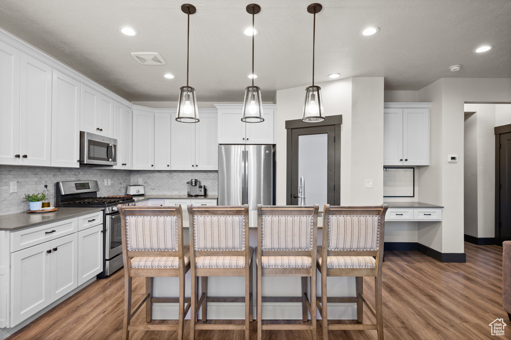 Kitchen with appliances with stainless steel finishes, a breakfast bar area, pendant lighting, and dark hardwood / wood-style flooring