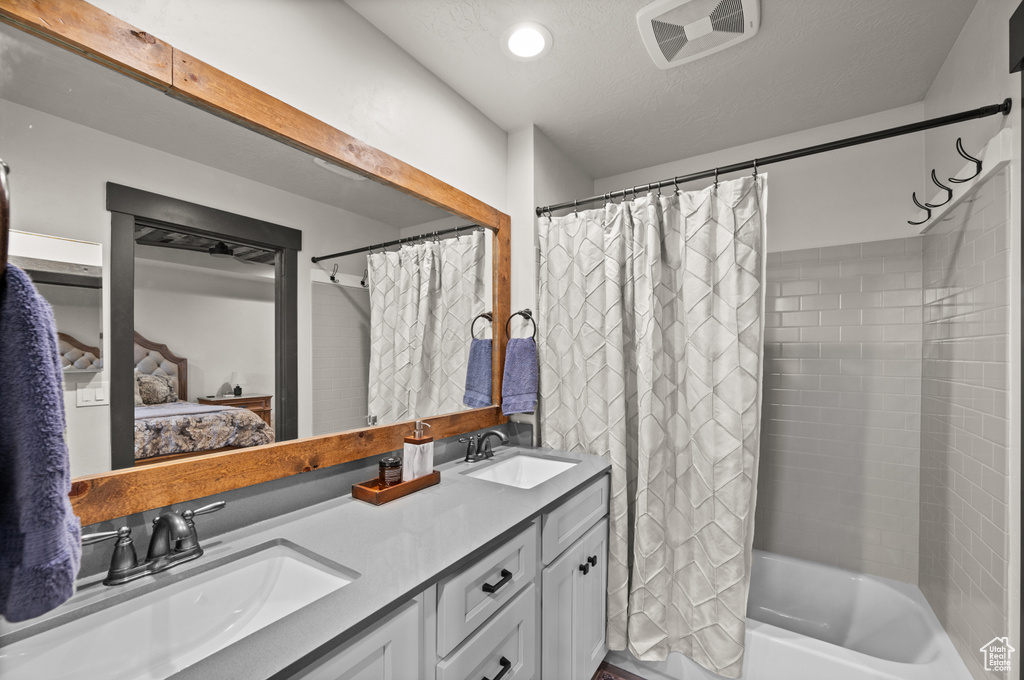 Bathroom with shower / bath combo, a textured ceiling, and dual vanity