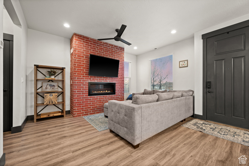 Living room with brick wall, light hardwood / wood-style flooring, ceiling fan, and a fireplace