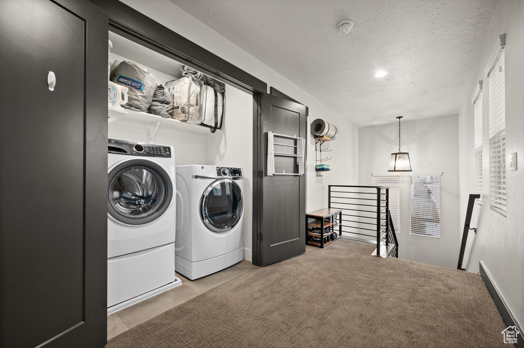 Clothes washing area featuring a textured ceiling, light colored carpet, and washer and clothes dryer