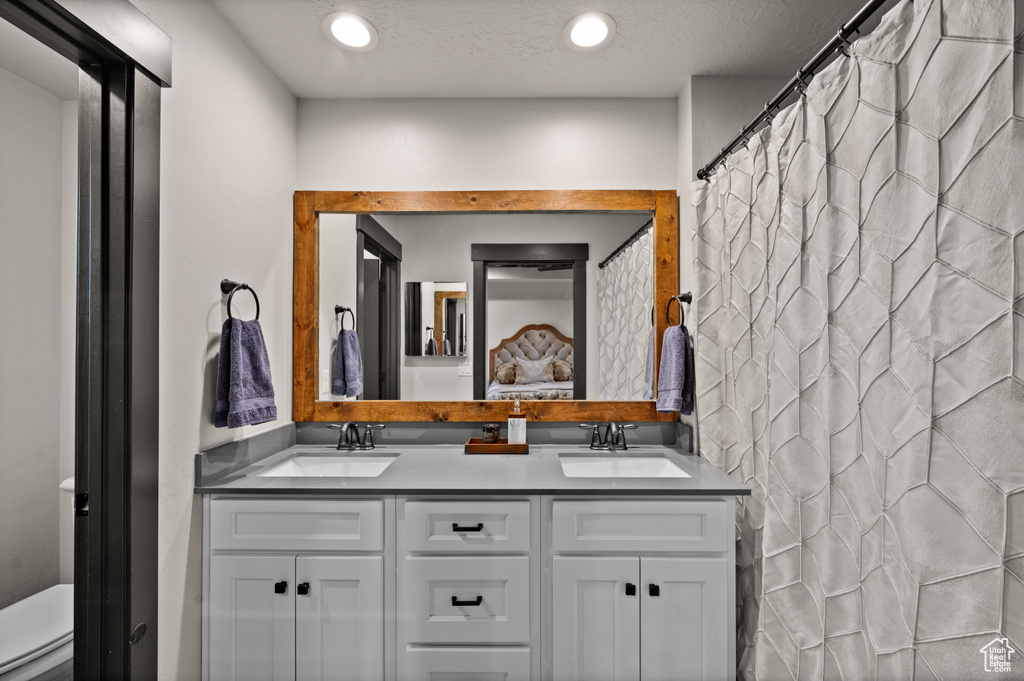 Bathroom featuring a textured ceiling, dual bowl vanity, and toilet