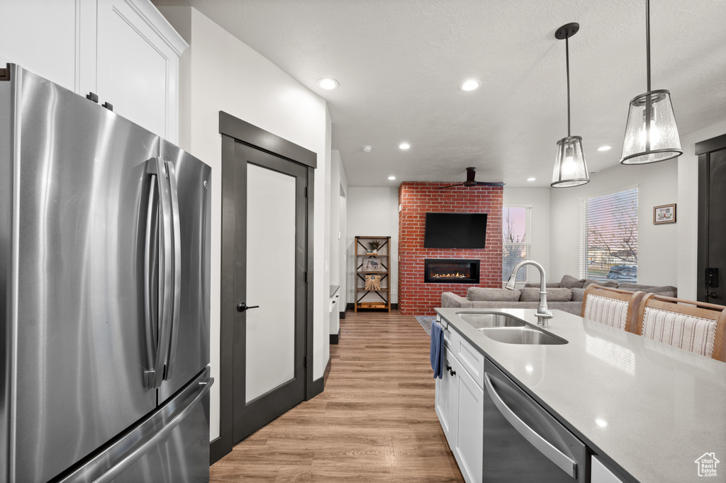 Kitchen featuring stainless steel appliances, white cabinets, decorative light fixtures, and light wood-type flooring