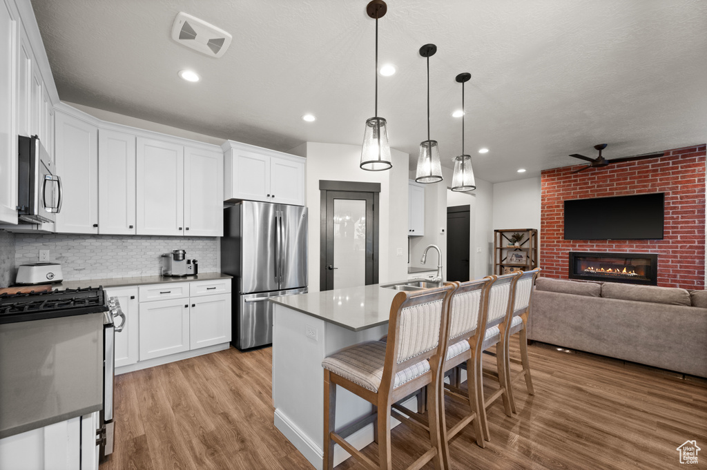 Kitchen with decorative light fixtures, appliances with stainless steel finishes, light hardwood / wood-style flooring, a brick fireplace, and white cabinets