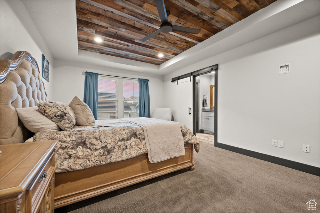 Carpeted bedroom with a barn door, ensuite bath, ceiling fan, wooden ceiling, and a raised ceiling