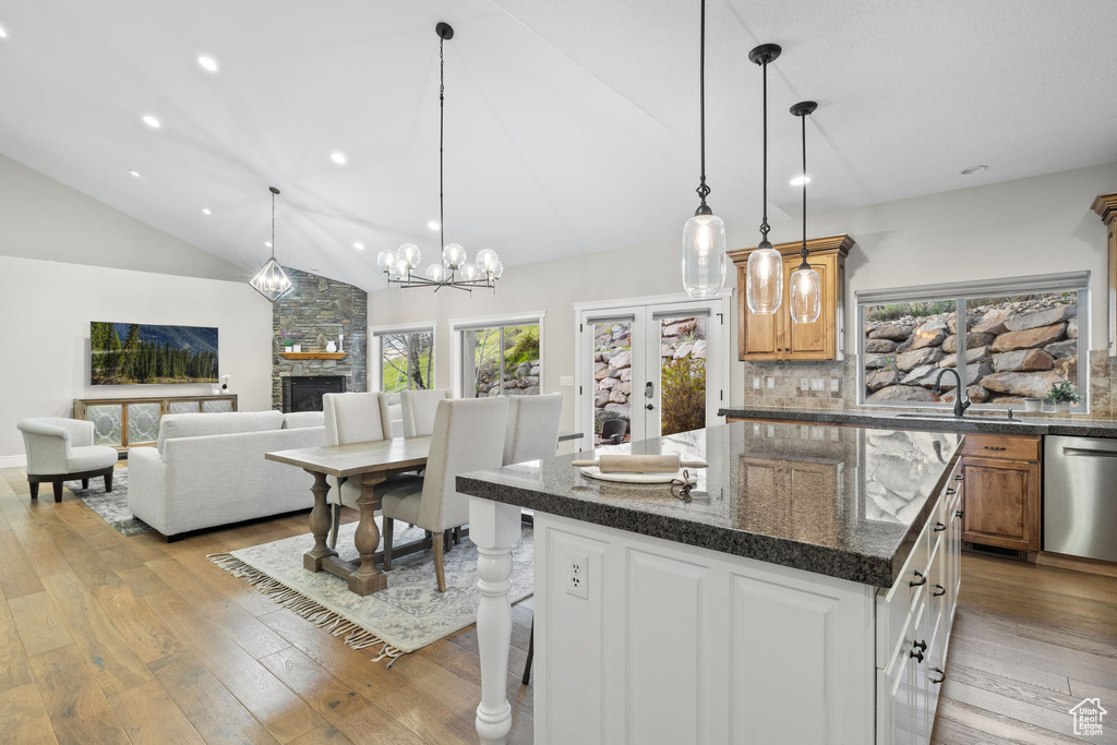 Kitchen featuring decorative light fixtures, a kitchen island, dishwasher, a fireplace, and light wood-type flooring