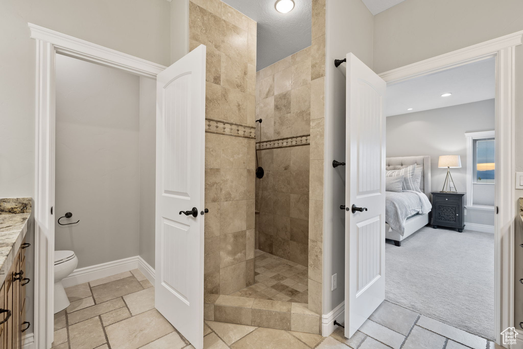 Bathroom featuring tile flooring, tiled shower, vanity, and toilet