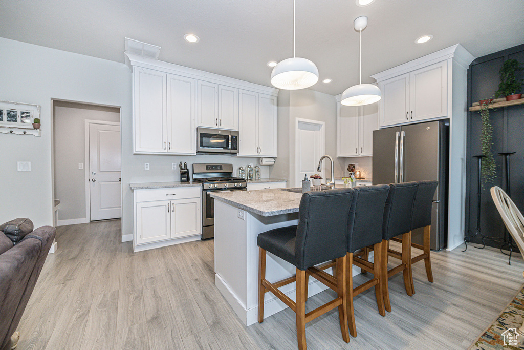 Kitchen featuring white cabinets, pendant lighting, stainless steel appliances, and light hardwood / wood-style floors