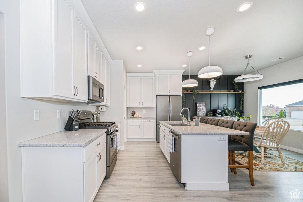 Kitchen with appliances with stainless steel finishes, hanging light fixtures, light hardwood / wood-style floors, white cabinets, and a kitchen breakfast bar