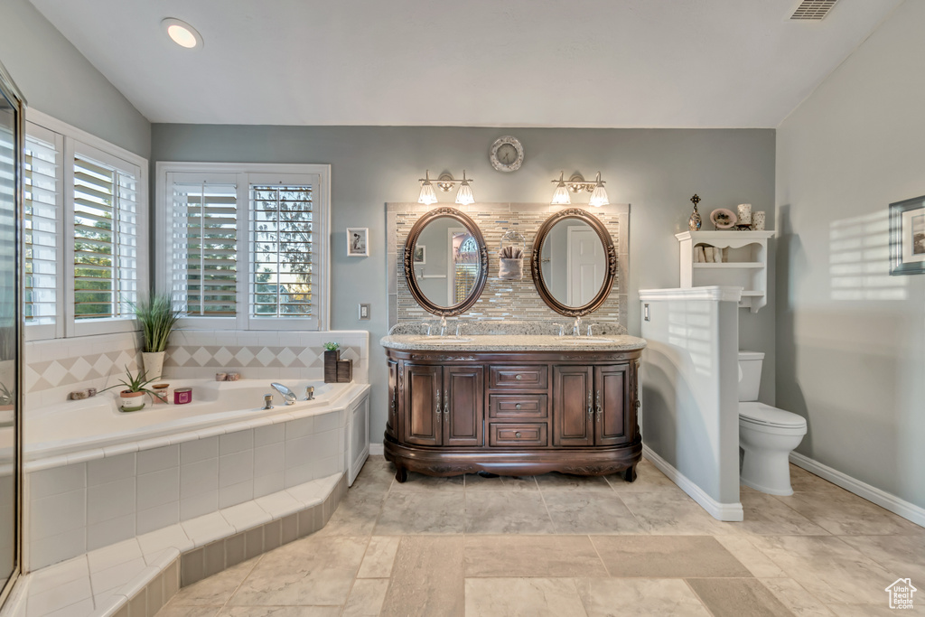 Bathroom featuring oversized vanity, toilet, tile flooring, a relaxing tiled bath, and dual sinks