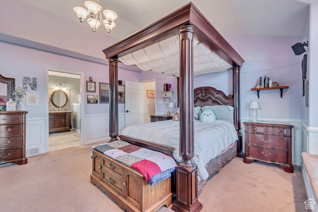 Carpeted bedroom featuring an inviting chandelier, vaulted ceiling, decorative columns, and ensuite bathroom