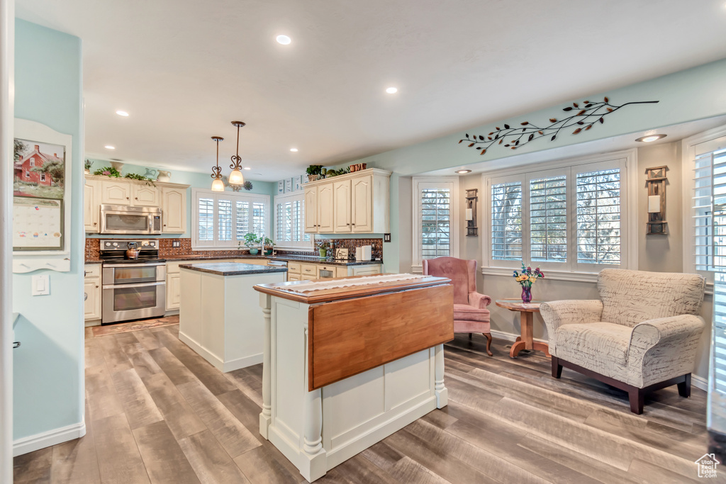 Kitchen featuring a center island, hanging light fixtures, appliances with stainless steel finishes, tasteful backsplash, and light hardwood / wood-style floors