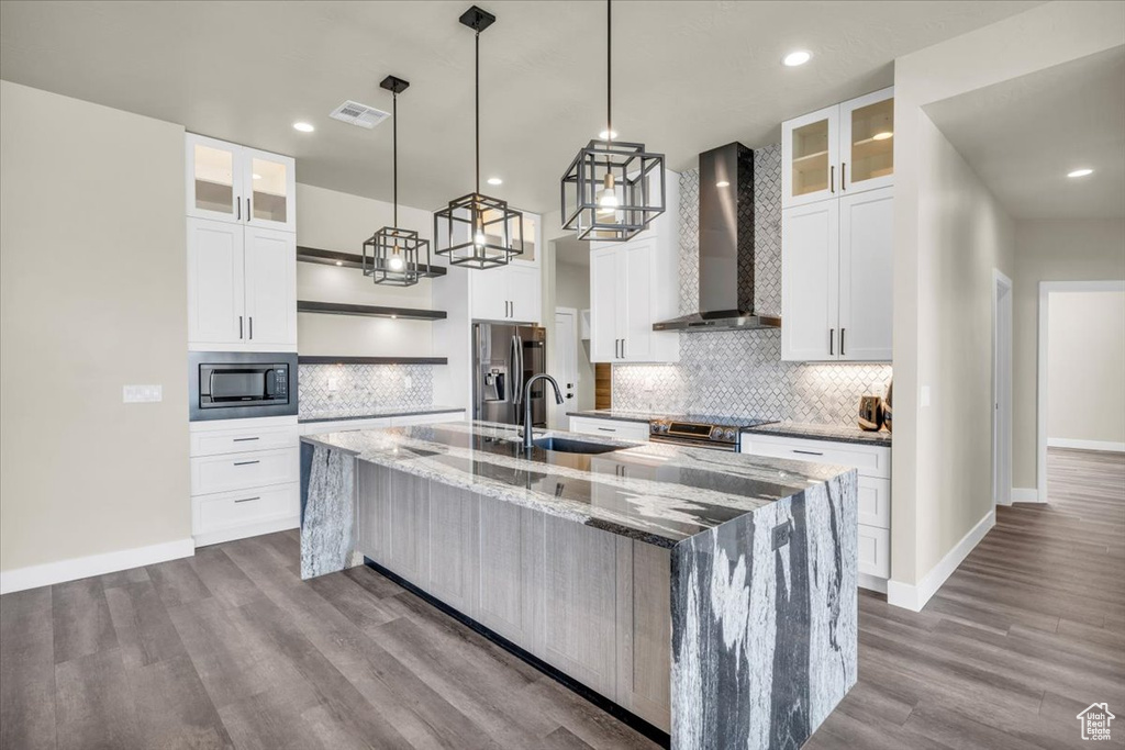 Kitchen featuring a center island with sink, wall chimney exhaust hood, white cabinetry, and appliances with stainless steel finishes