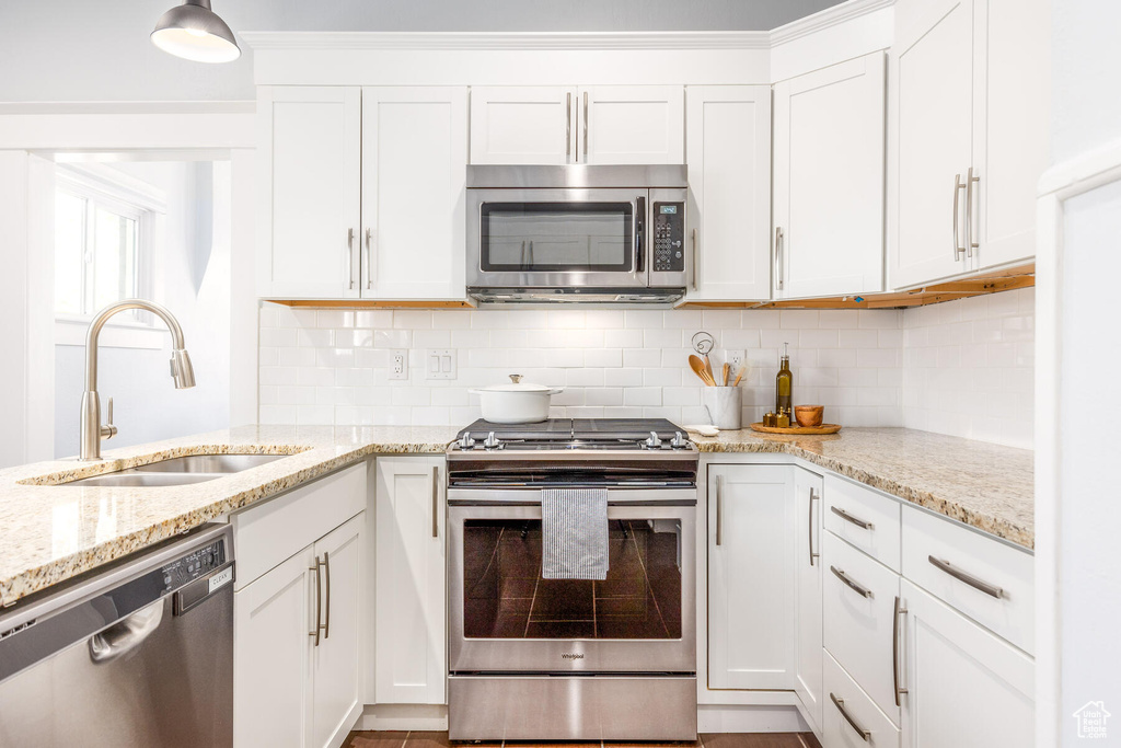 Kitchen featuring tasteful backsplash, appliances with stainless steel finishes, white cabinetry, and light stone countertops