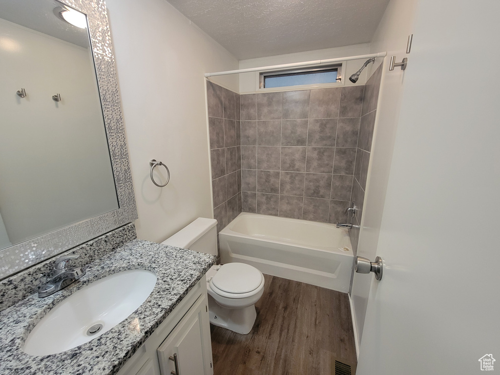 Full bathroom with tiled shower / bath, a textured ceiling, toilet, vanity, and hardwood / wood-style flooring