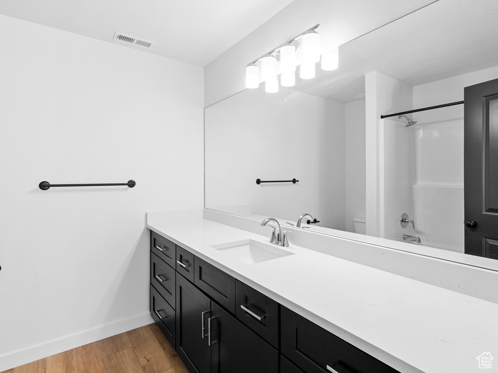 Full bathroom with vanity with extensive cabinet space, toilet, hardwood / wood-style floors, and  shower combination