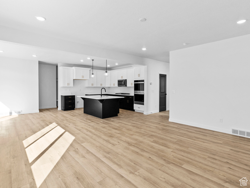 Kitchen featuring a kitchen island with sink, white cabinets, sink, light wood-type flooring, and pendant lighting