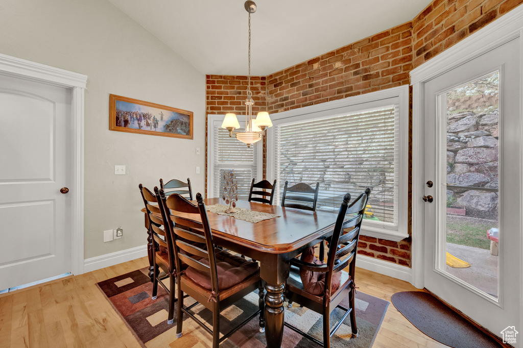 Dining space featuring brick wall, light wood-type flooring, a notable chandelier, and lofted ceiling