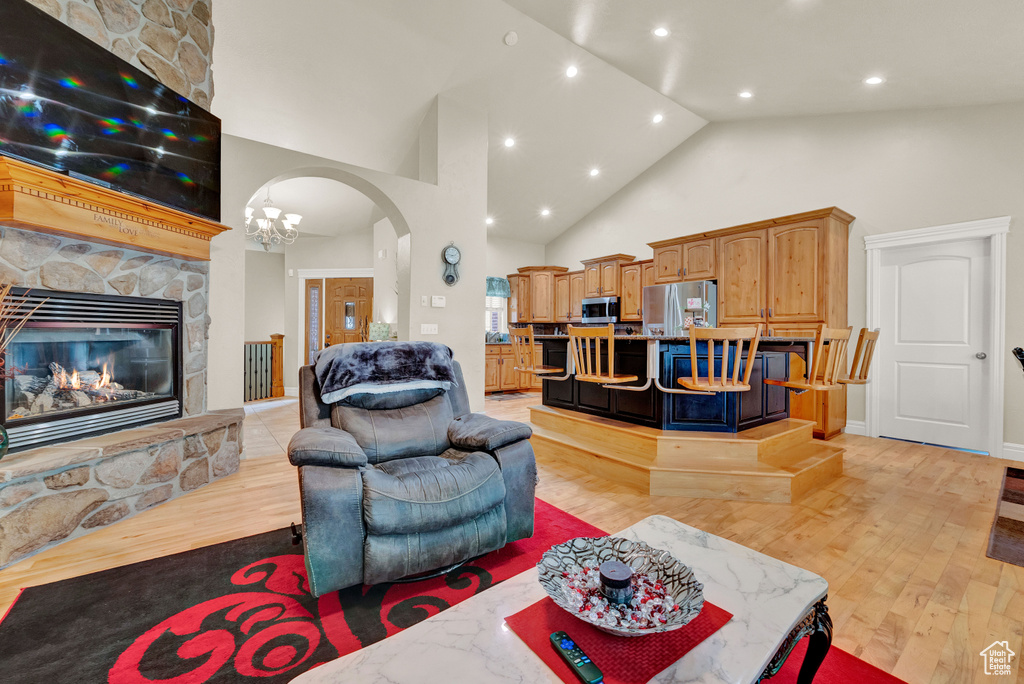 Living room featuring high vaulted ceiling, a notable chandelier, light hardwood / wood-style flooring, and a stone fireplace