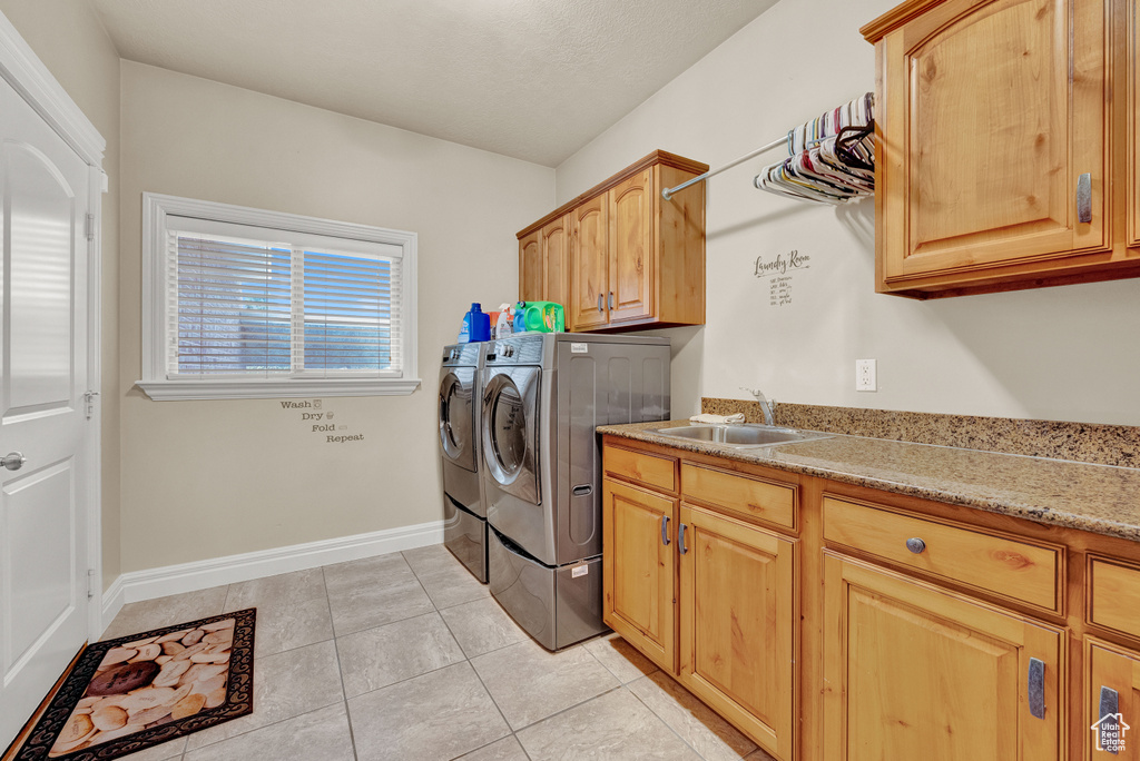 Clothes washing area with cabinets, sink, washing machine and dryer, and light tile flooring