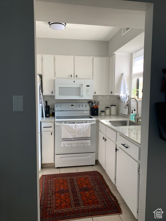 Kitchen with white cabinets, sink, white appliances, tasteful backsplash, and light tile flooring