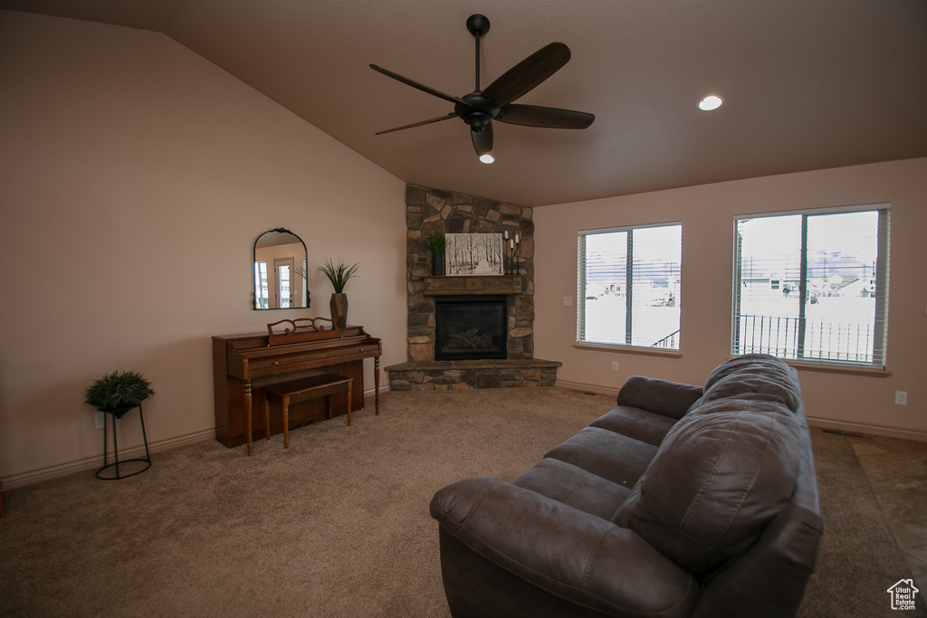Carpeted living room with a stone fireplace, ceiling fan, and lofted ceiling