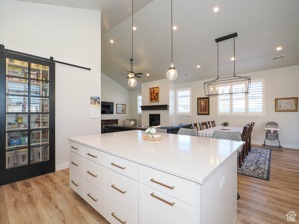 Kitchen featuring pendant lighting, white cabinets, a large fireplace, and light wood-type flooring