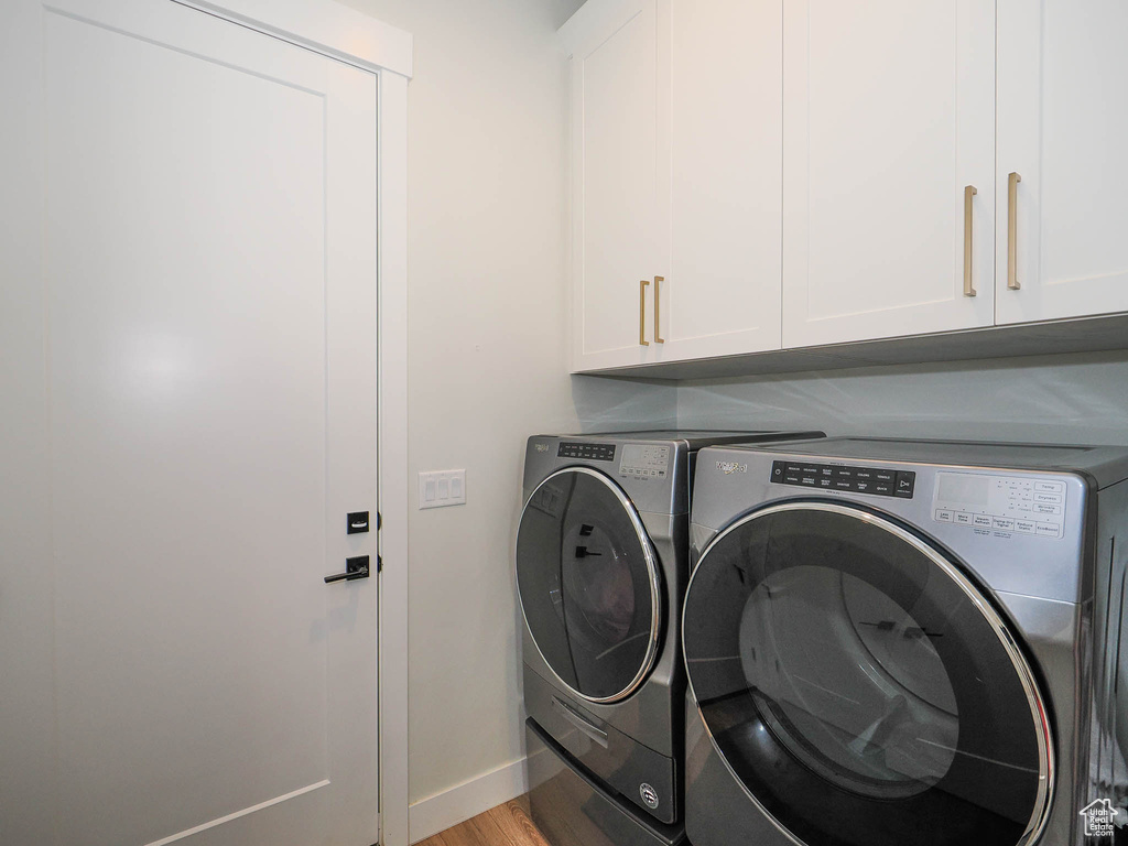 Laundry room featuring washing machine and clothes dryer, cabinets, and light wood-type flooring