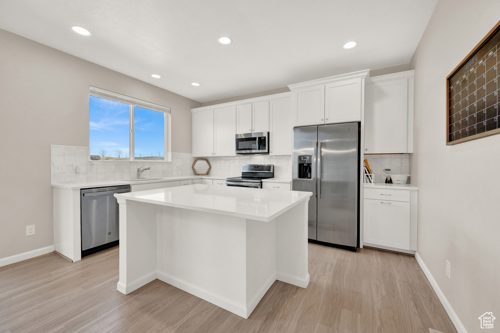 Kitchen with appliances with stainless steel finishes, a kitchen island, backsplash, light hardwood / wood-style floors, and white cabinetry
