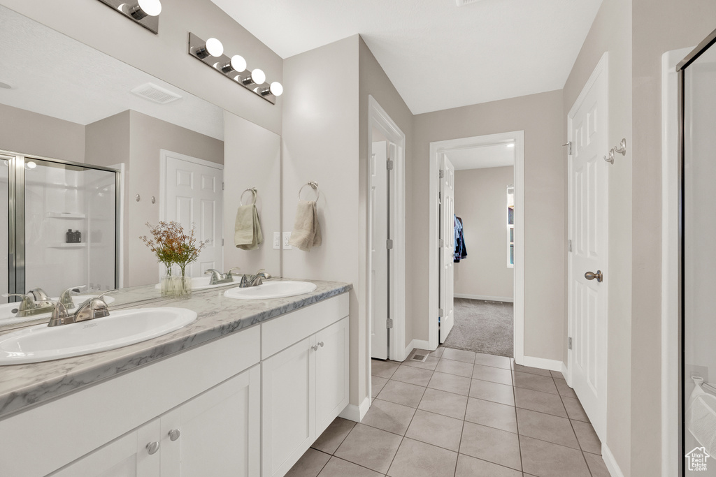Bathroom featuring vanity with extensive cabinet space, double sink, tile flooring, and a shower with door