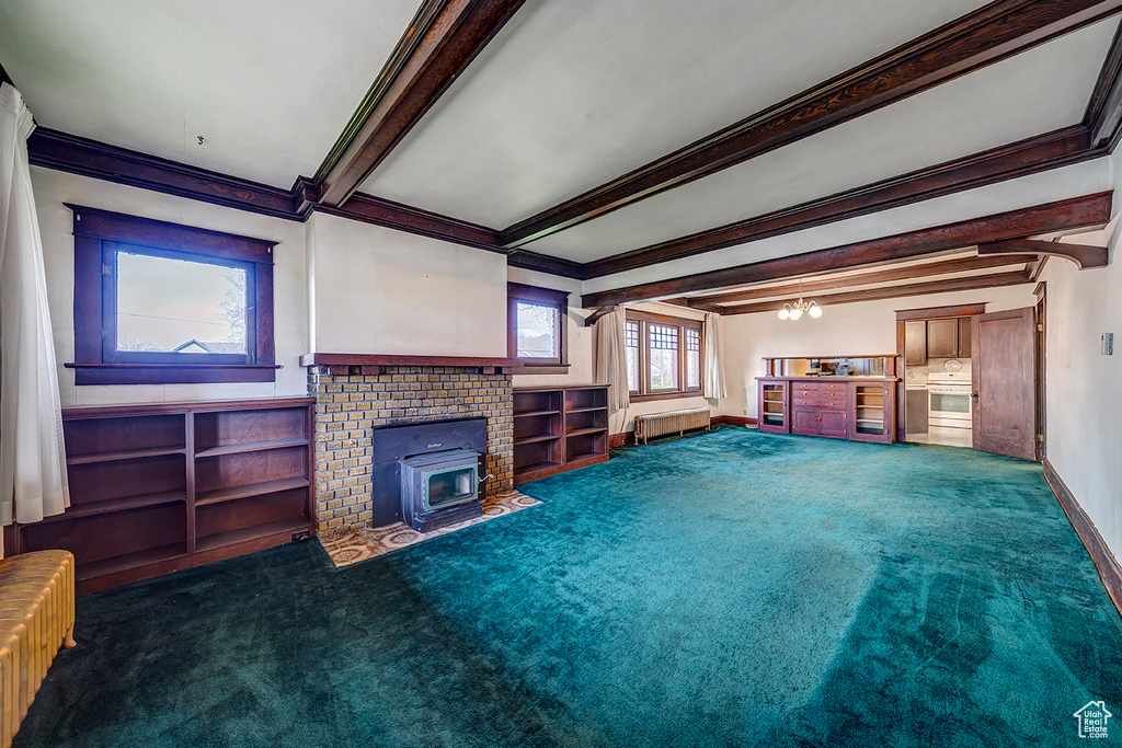 Unfurnished living room featuring dark carpet, beamed ceiling, a fireplace, ornamental molding, and radiator heating unit