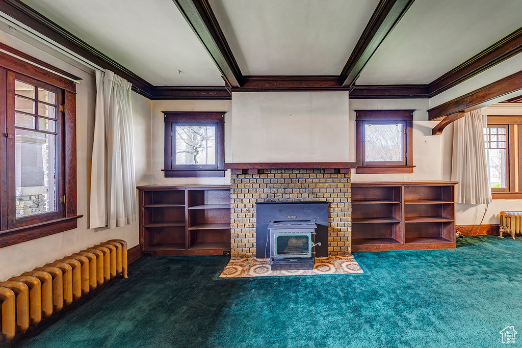 Unfurnished living room featuring beam ceiling, radiator heating unit, a fireplace, and dark colored carpet